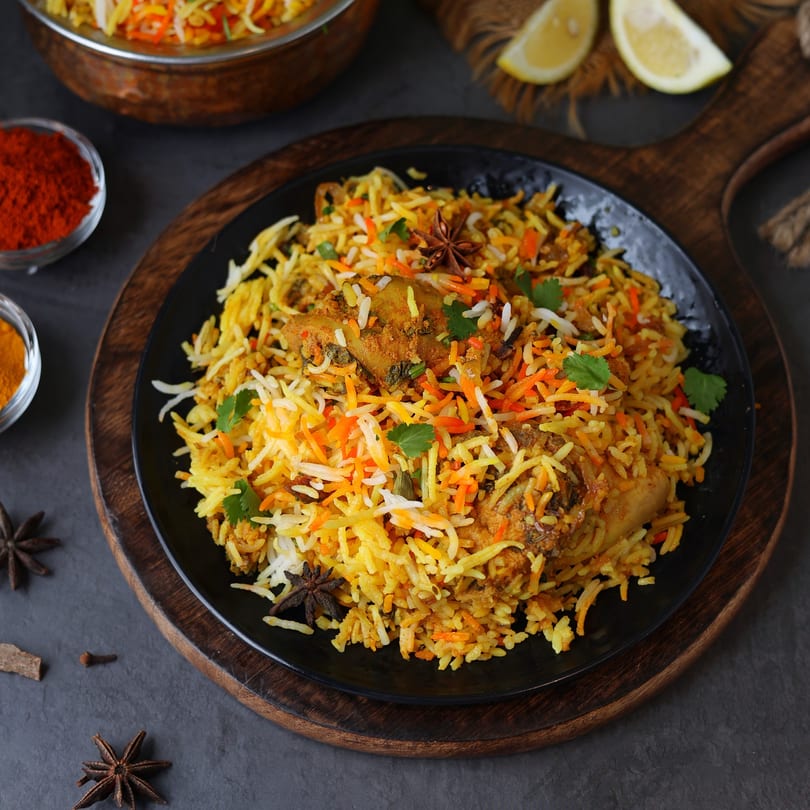 A black plate of Anu's Indian Bar and Grill chicken biryani, garnished with cilantro and star anise.