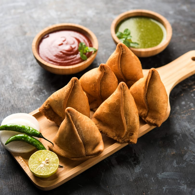 Golden-brown Anu's Indian Bar and Grill samosas with green and red chutneys, lime, onions, and chilies.