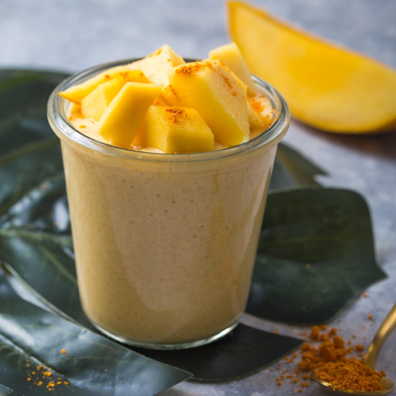 Mango lassi in a glass, topped with fresh mango chunks and a sprinkle of turmeric.
